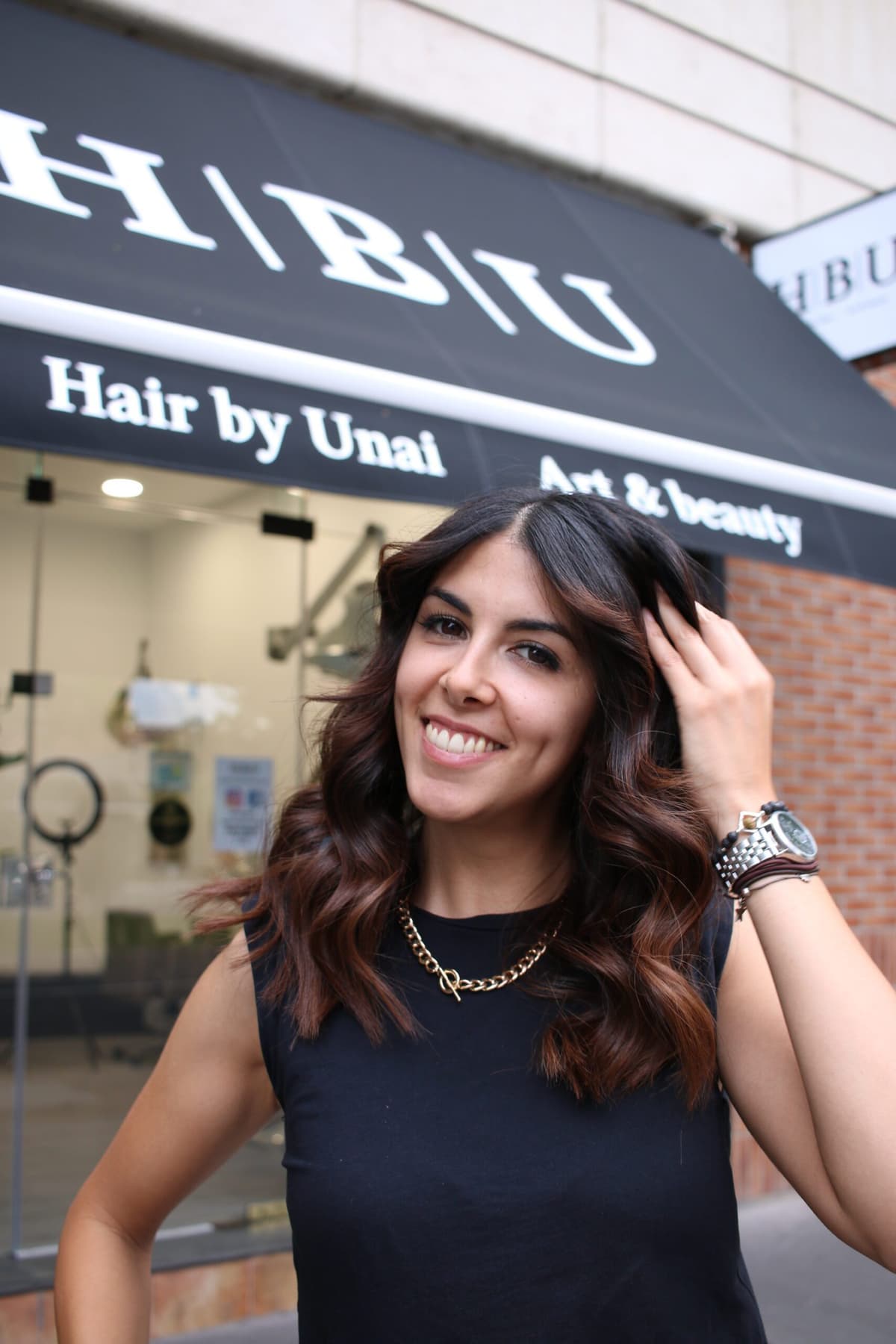 Clienta sonriente en la fachada de Peluquería HBU Hair By Unai